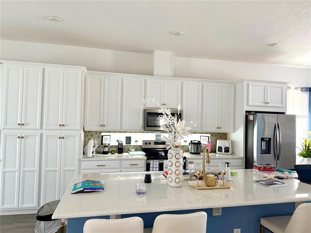 A kitchen features white cabinetry, a quartz-topped island, stainless steel appliances, and a blue base — 13456 LAXNESS STREET, ORLANDO, FL