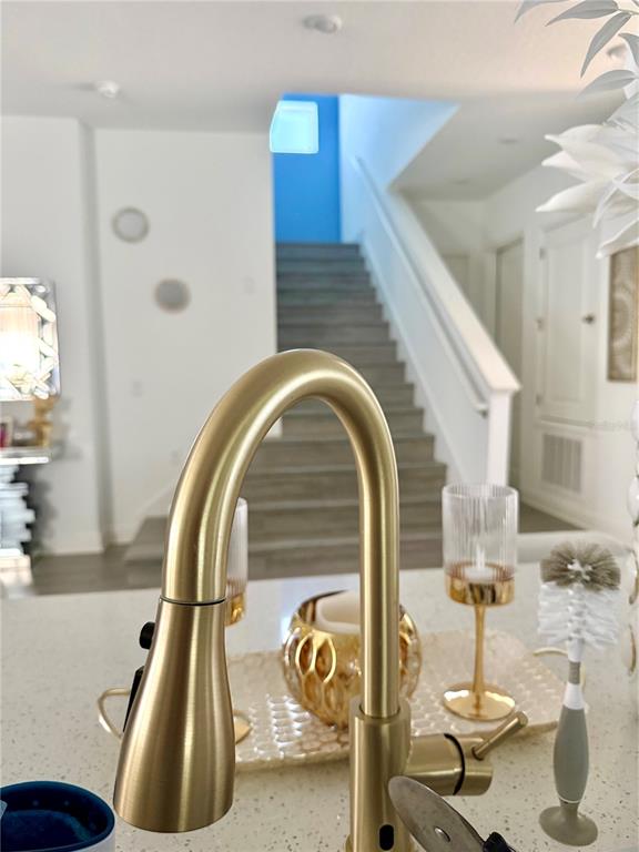 A gold kitchen faucet sits on a white countertop with a staircase in the background — 13456 LAXNESS STREET, ORLANDO, FL