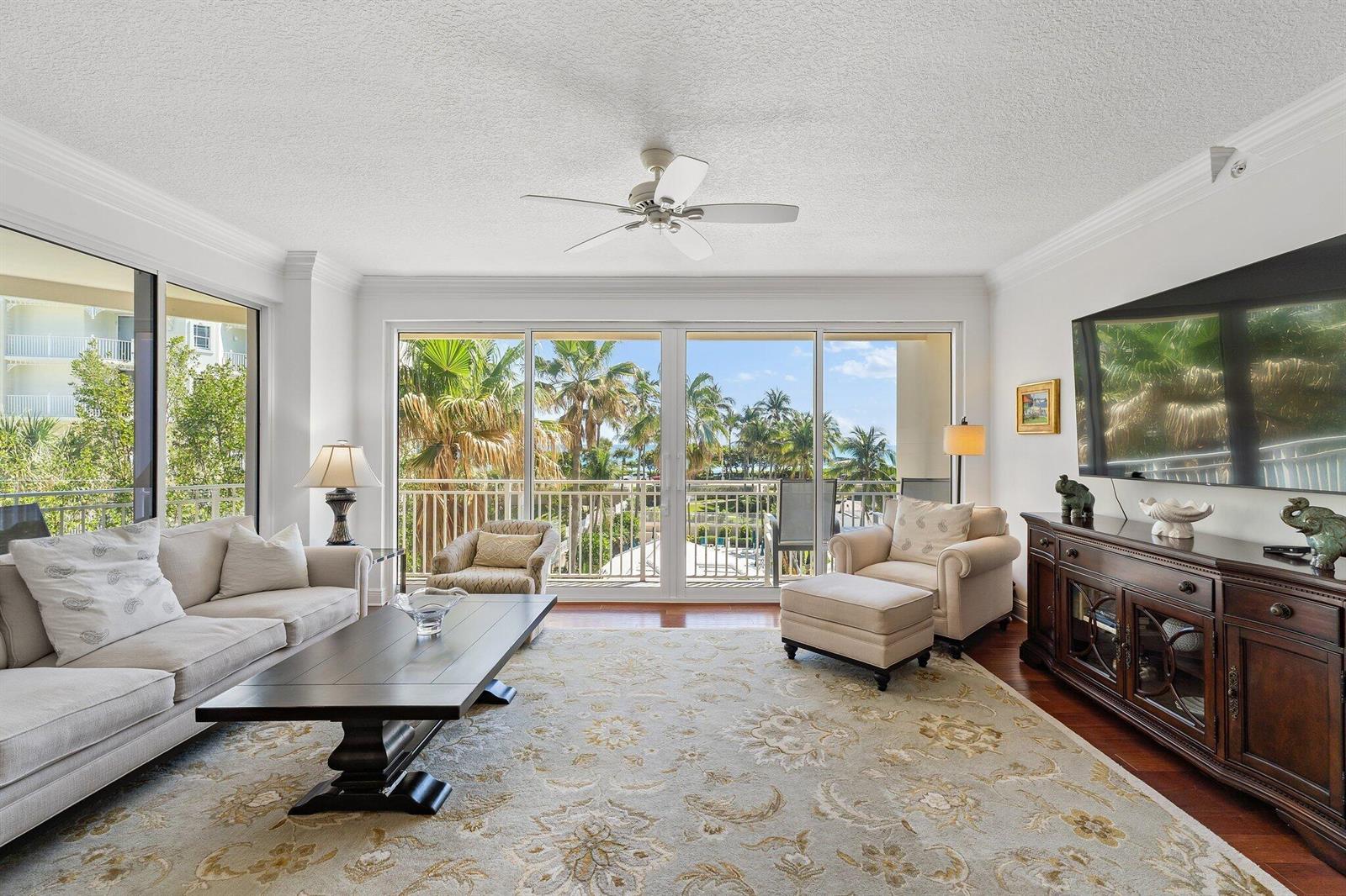 A living room features a beige sofa, patterned area rug, and sliding glass doors overlooking palm trees — 1660 S Hwy A1a # 122, Jupiter FL 33477, JUPITER, FL