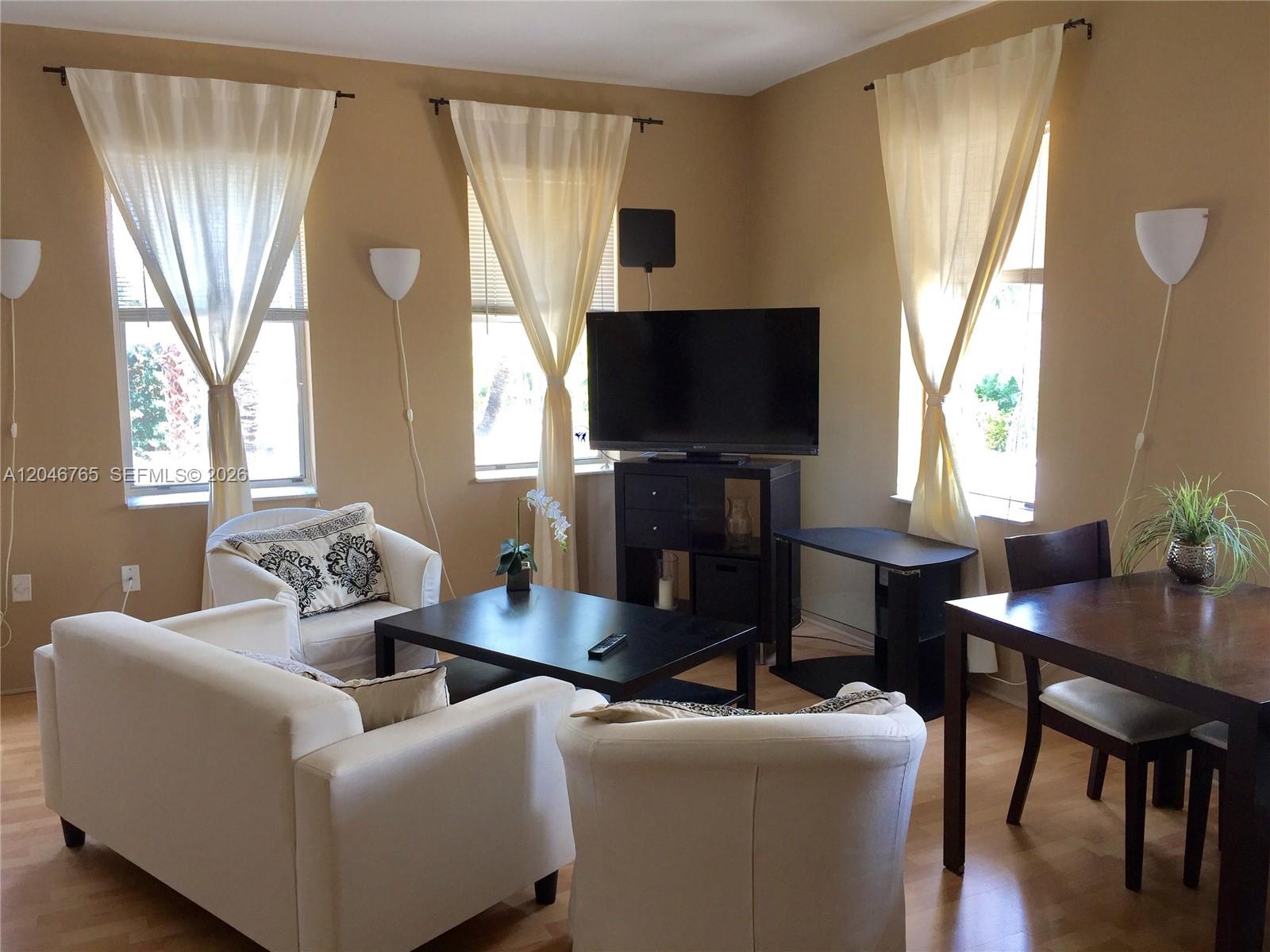 A living room features white furniture, a black coffee table, a television, and three windows — 802 Euclid Ave # 201, Miami Beach FL 33139, MIAMI BEACH, FL