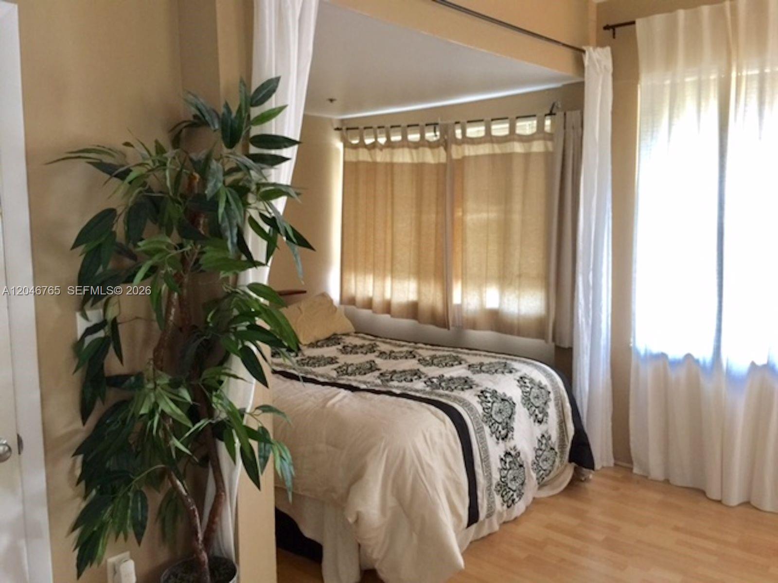 A bedroom features a bed tucked into an alcove with tan curtains and light wood flooring — 802 Euclid Ave # 201, Miami Beach FL 33139, MIAMI BEACH, FL
