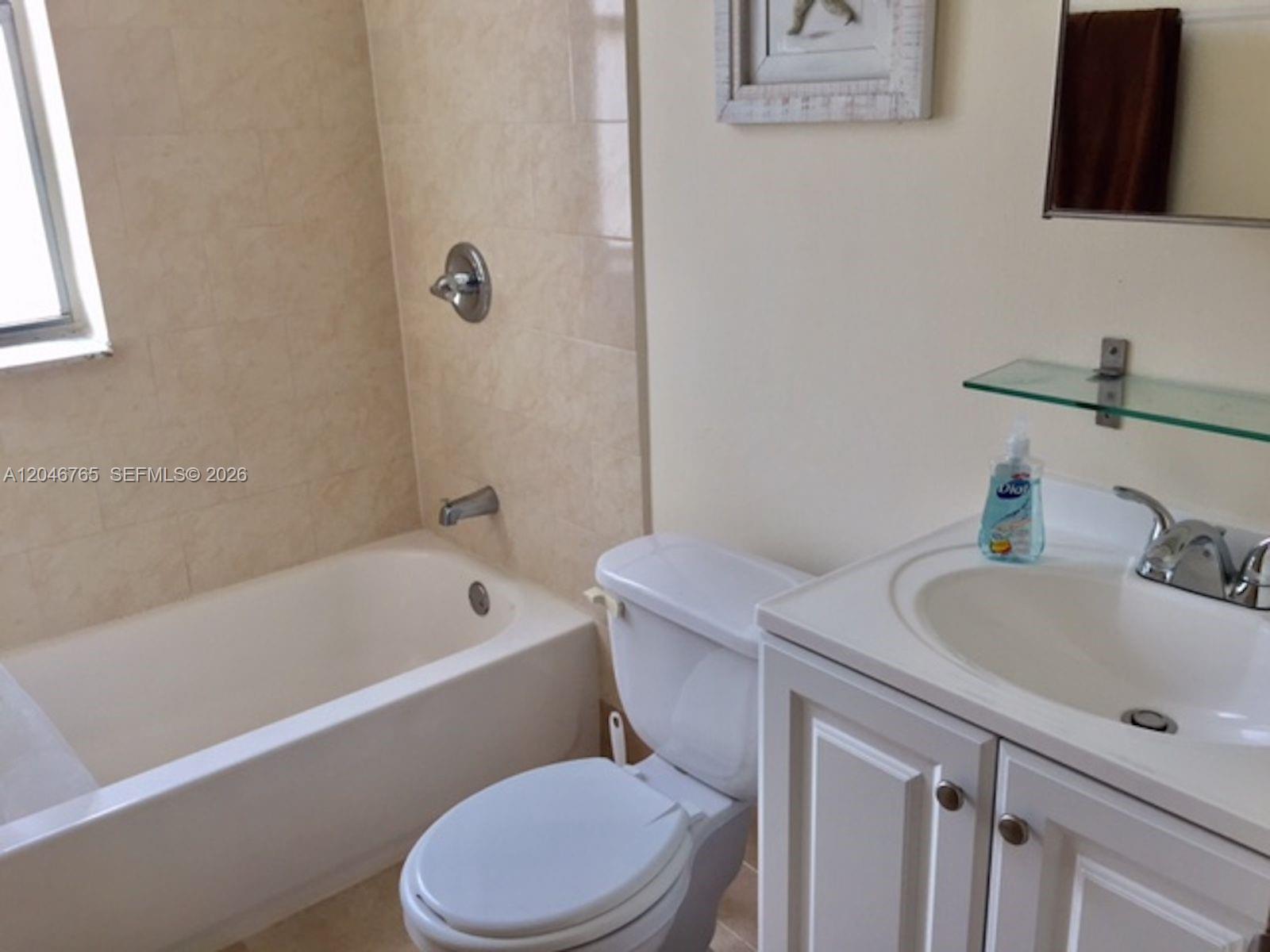 A bathroom features a white vanity, a toilet, and a bathtub with beige tile walls — 802 Euclid Ave # 201, Miami Beach FL 33139, MIAMI BEACH, FL