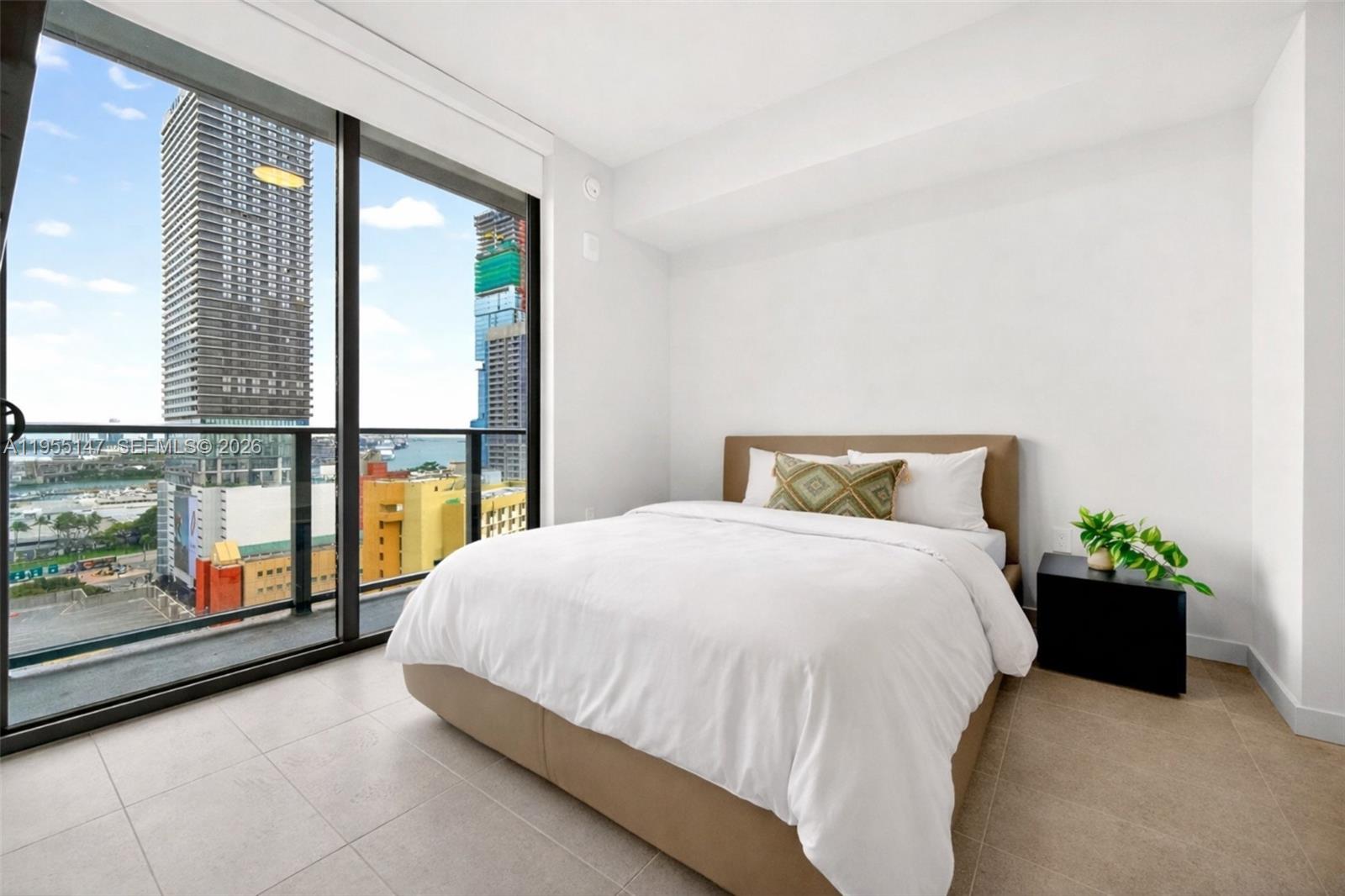 A bedroom with a bed, a black nightstand, and floor-to-ceiling windows overlooking a city skyline — 121 NE 5th Street # 1913, Miami FL 33132, MIAMI, FL