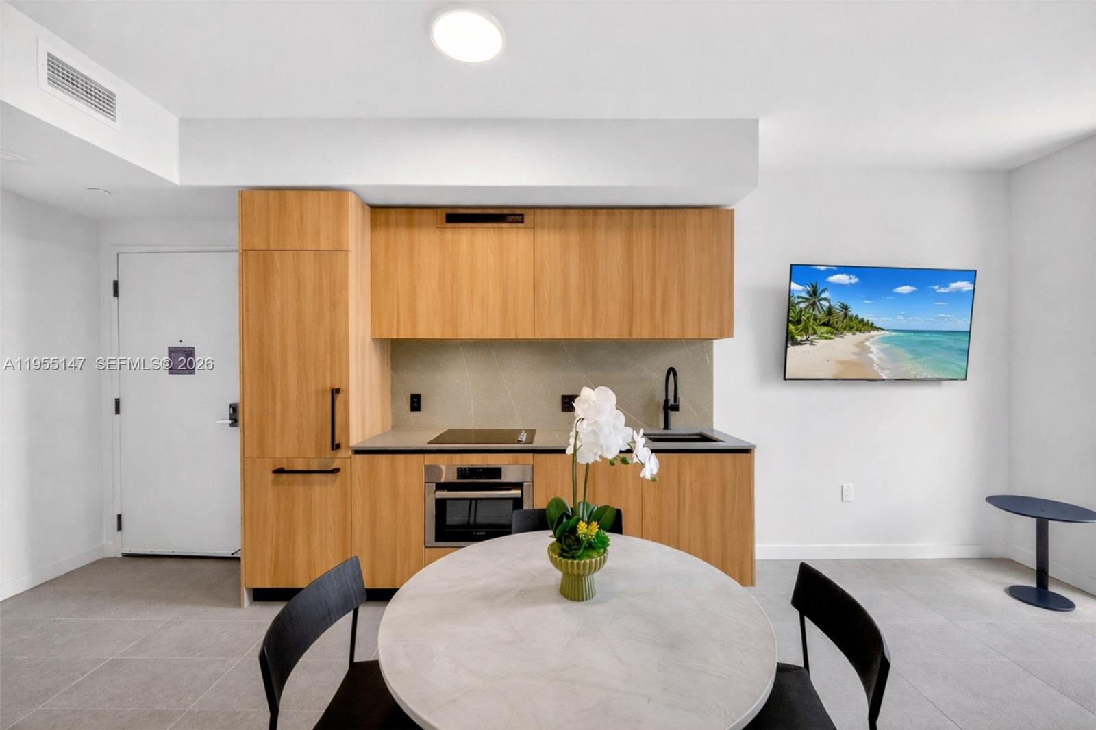 A modern kitchen features light wood cabinetry, a round dining table, and a wall-mounted television — 121 NE 5th Street # 1913, Miami FL 33132, MIAMI, FL