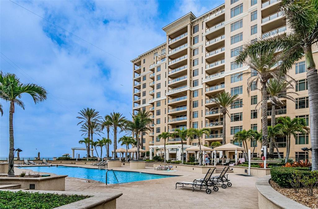 A multi-story residential building overlooks a swimming pool surrounded by palm trees and lounge chairs — 11 BAYMONT STREET UNIT 608, CLEARWATER BEACH, FL