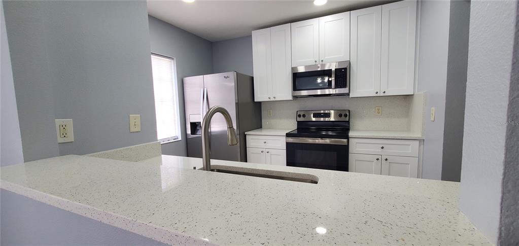 A kitchen features white cabinets, stainless steel appliances, and a speckled white countertop — 1661 FLUORSHIRE DRIVE, BRANDON, FL