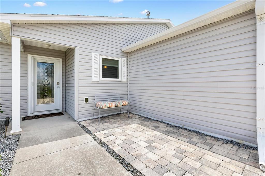 A light gray vinyl-sided house exterior features a front door, a window, and a patio — 470 OBOE WAY, THE VILLAGES, FL