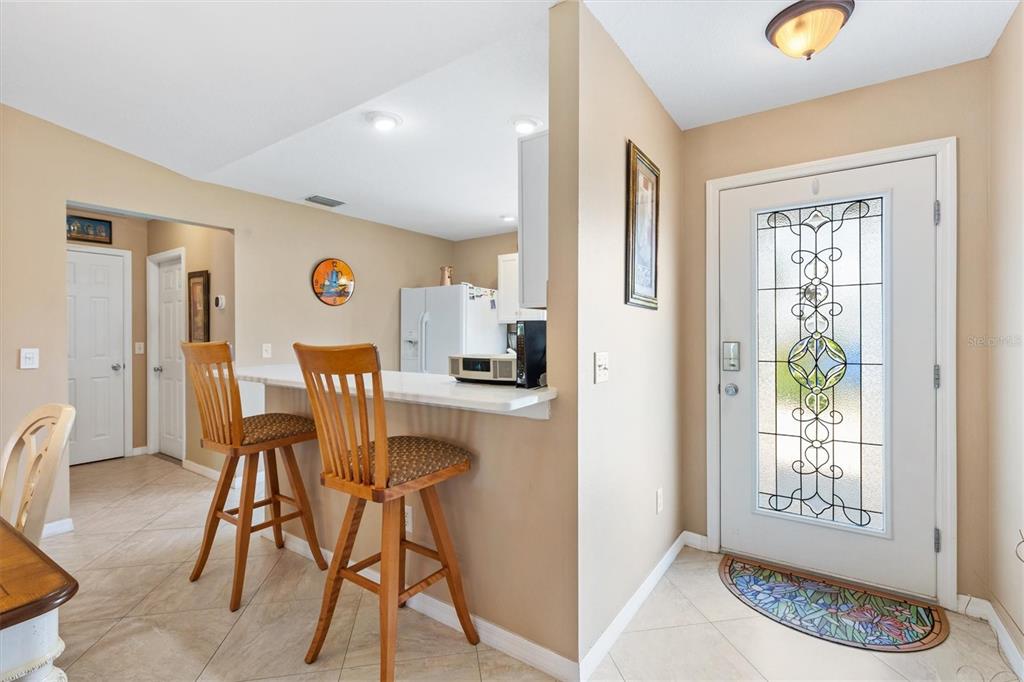 A kitchen breakfast bar with two wooden stools sits near an entryway with a decorative door — 470 OBOE WAY, THE VILLAGES, FL