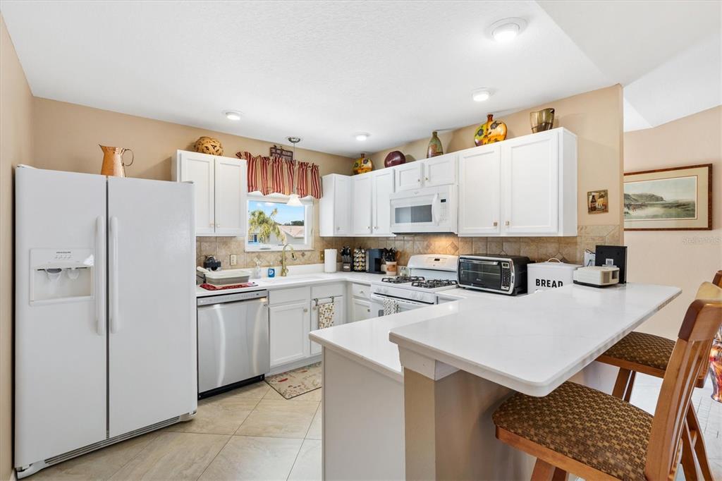 A kitchen with white cabinets, stainless steel appliances, and a breakfast bar with stools — 470 OBOE WAY, THE VILLAGES, FL