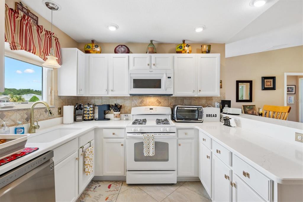 A kitchen features white cabinets, white countertops, a white stove, and a stainless steel dishwasher — 470 OBOE WAY, THE VILLAGES, FL