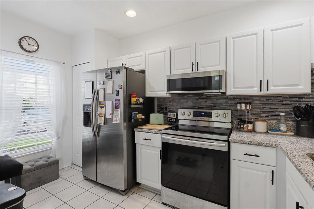 A kitchen features white cabinets, stainless steel appliances, granite countertops, and a tiled backsplash — 30029 GRANDA HILLS COURT, WESLEY CHAPEL, FL