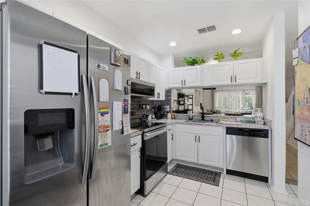 A kitchen features white cabinets, stainless steel appliances, a tiled floor, and a pass-through window — 30029 GRANDA HILLS COURT, WESLEY CHAPEL, FL