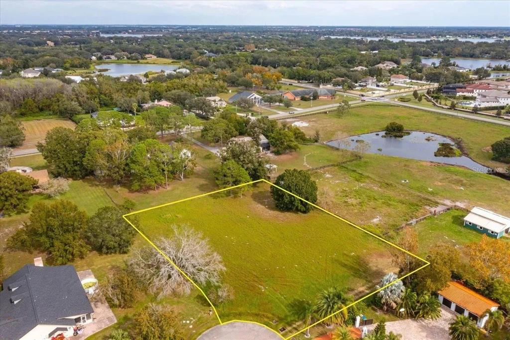 An aerial view shows a vacant, grassy residential lot outlined in yellow near a pond — 13125 FILLY COURT, WINDERMERE, FL