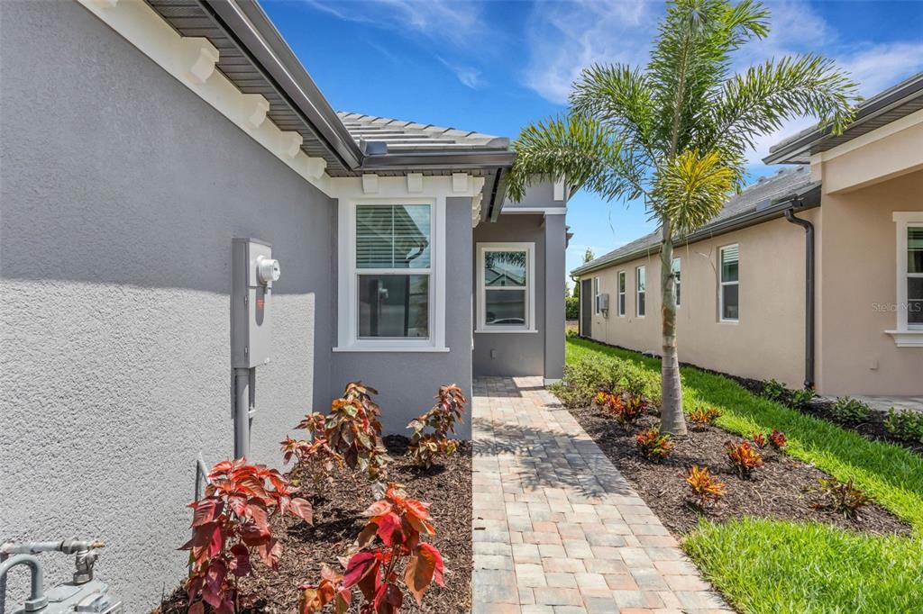 A paved walkway leads between two single-story houses with landscaped garden beds and a palm tree — 18181 CHERISHED LOOP, BRADENTON, FL
