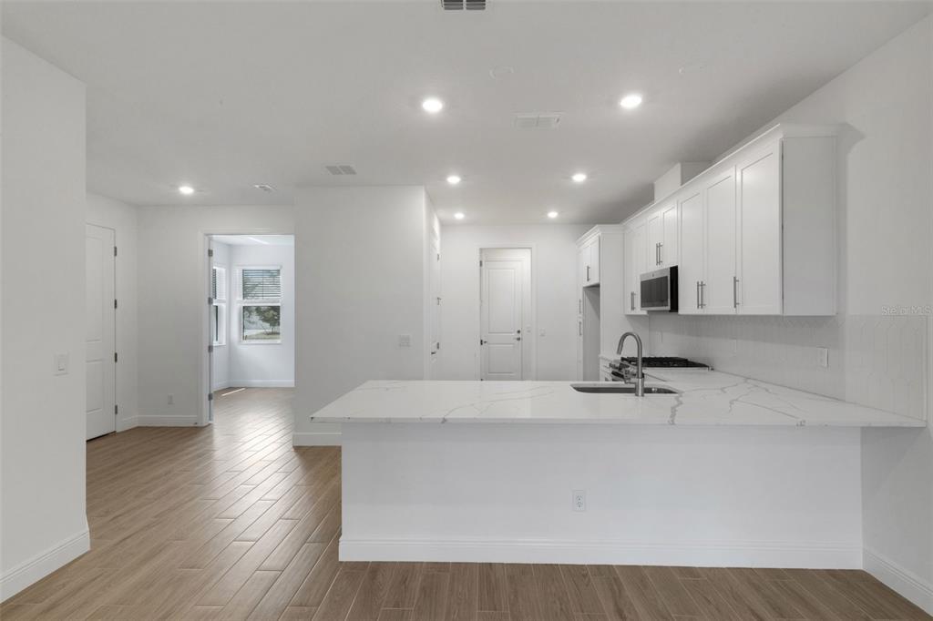 A modern kitchen features white cabinets, a marble-look island, and light wood-style flooring — 18181 CHERISHED LOOP, BRADENTON, FL