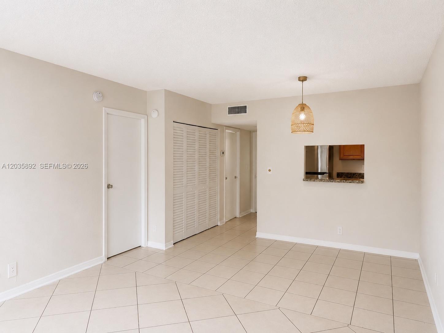 An empty room features beige walls, light-colored tile flooring, a closet, and a pass-through window — 280 S Cypress Rd # 310, Pompano Beach FL 33060, POMPANO BEACH, FL