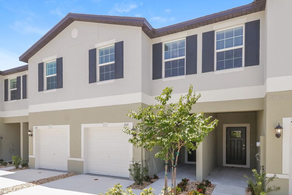 A two-story townhouse exterior features a white garage, a recessed entryway, and dark shutters — 2145 GREAT SAPPHIRE LANE, LUTZ, FL