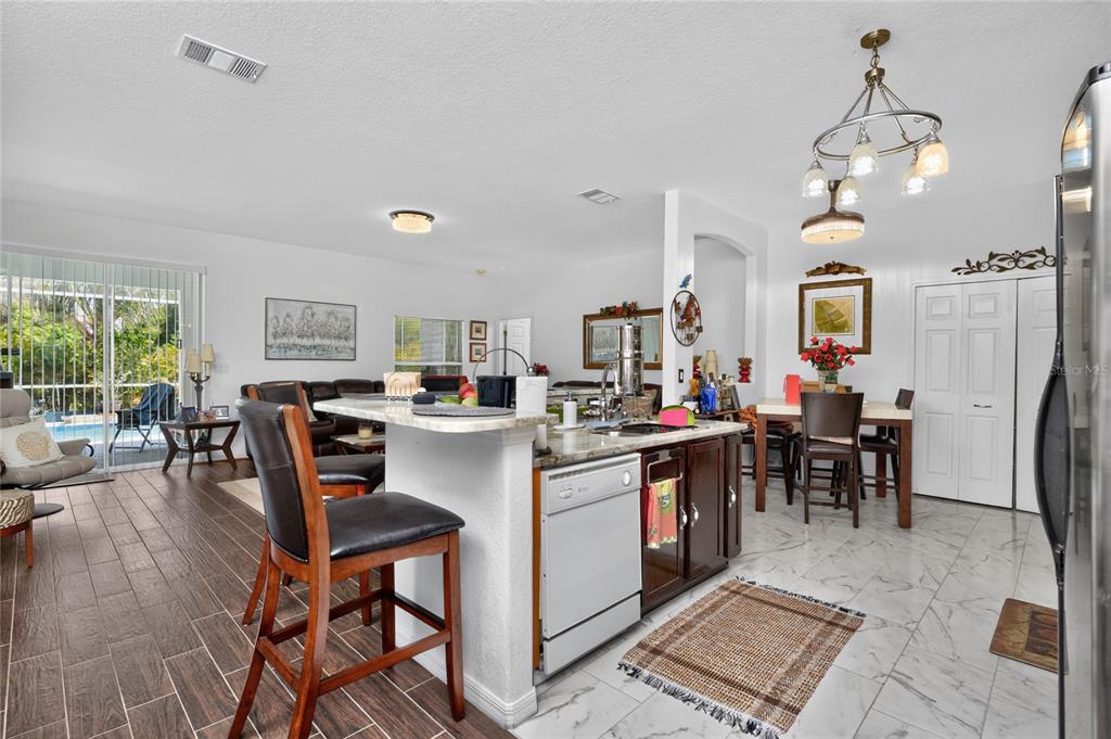 A kitchen with a granite-topped island and bar seating overlooks a dining area and living room — 25324 ALICANTE DRIVE, PUNTA GORDA, FL