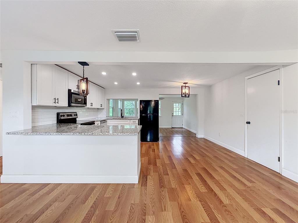 A kitchen with white cabinets, granite countertops, and hardwood floors opens to a dining area — 6845 MEDLAR DRIVE, NEW PORT RICHEY, FL