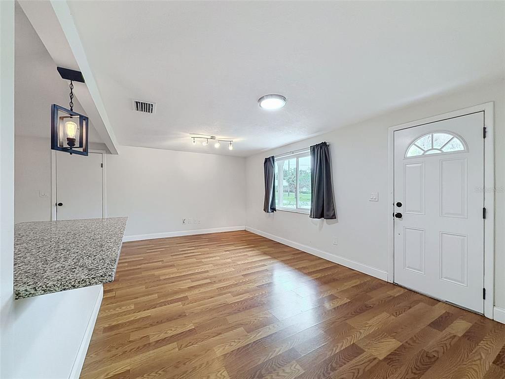 A living room with wood-look flooring, a granite breakfast bar, and a white front door — 6845 MEDLAR DRIVE, NEW PORT RICHEY, FL