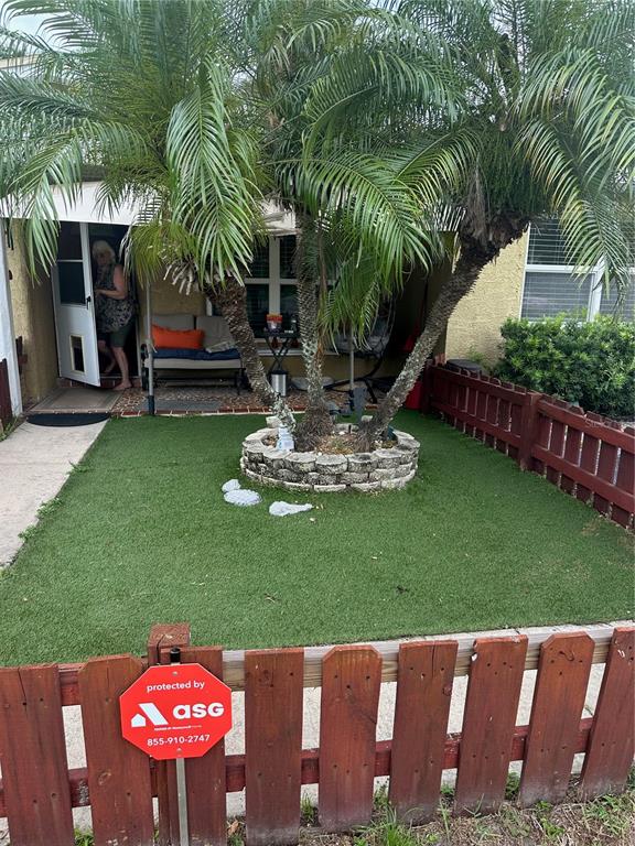 A small front yard with artificial turf, a palm tree in a stone planter, and fencing — 721 OLEANDER WAY S, SOUTH PASADENA, FL