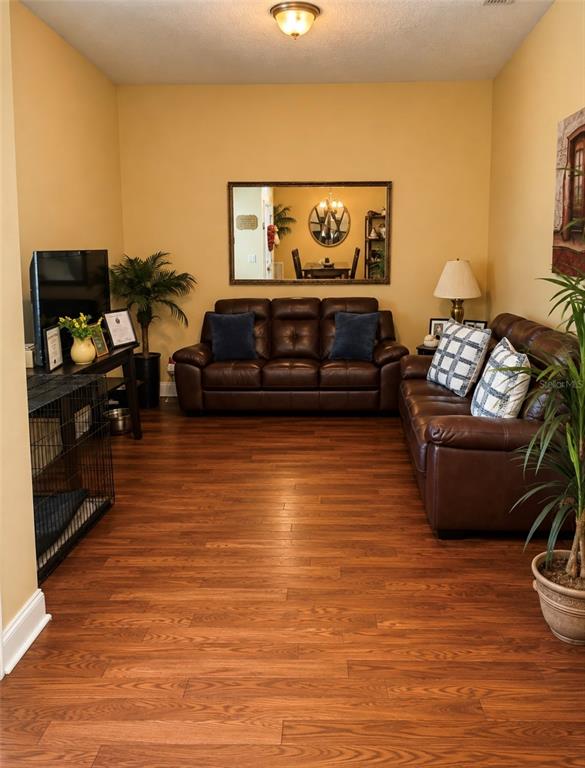 A living room features a dark leather sofa, a television console, and wood-look flooring — 3 RAE JUNE PLACE, PALM COAST, FL