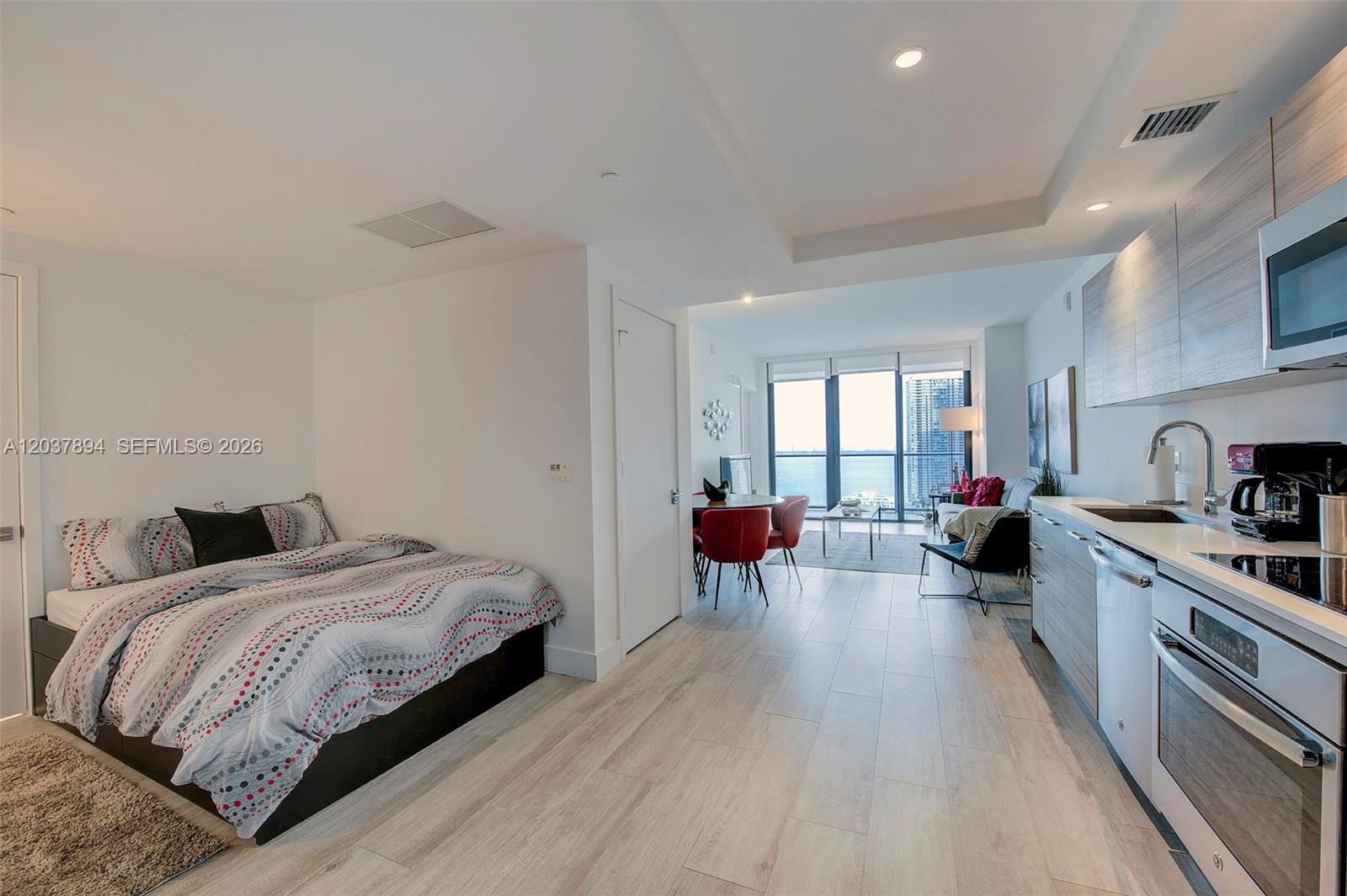 A studio apartment features a bed, a kitchenette, and a living area with floor-to-ceiling windows — 121 NE 34th St # 3006, Miami FL 33137, MIAMI, FL
