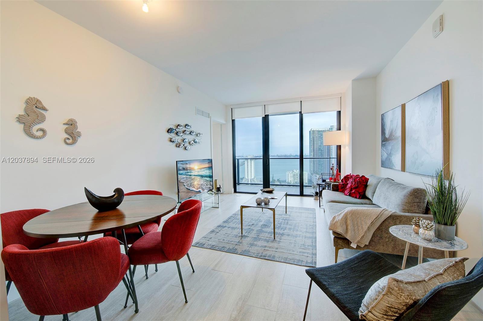 A living and dining area features red chairs, a gray sofa, and floor-to-ceiling windows — 121 NE 34th St # 3006, Miami FL 33137, MIAMI, FL