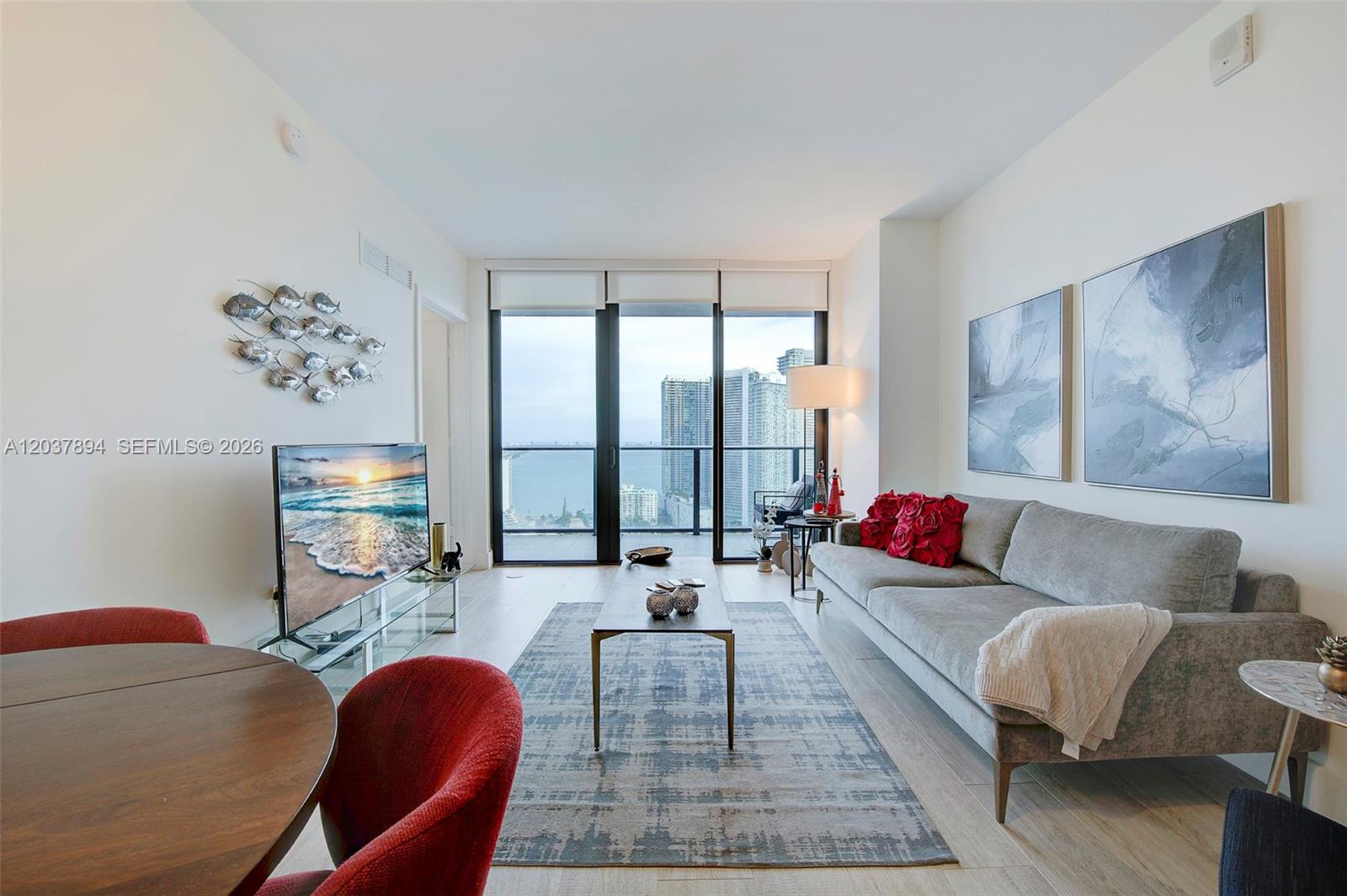 A living room features a grey sofa, a coffee table, and a balcony with city views — 121 NE 34th St # 3006, Miami FL 33137, MIAMI, FL