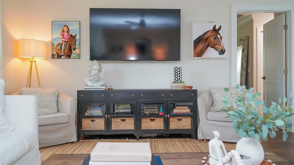 A living room features a television above a black media console between two armchairs — 5218 VENETIAN BOULEVARD NE, ST PETERSBURG, FL