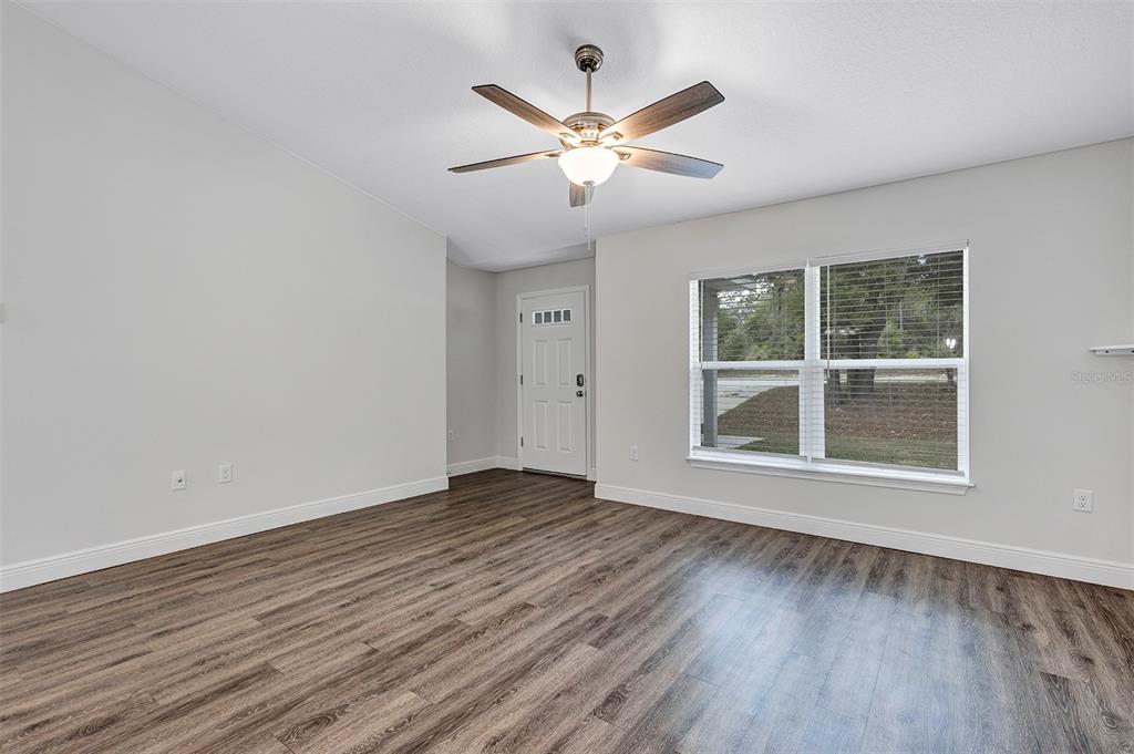 An empty room with wood-look flooring, a ceiling fan, and a white front door — 9219 N ELKCAM BOULEVARD, CITRUS SPRINGS, FL