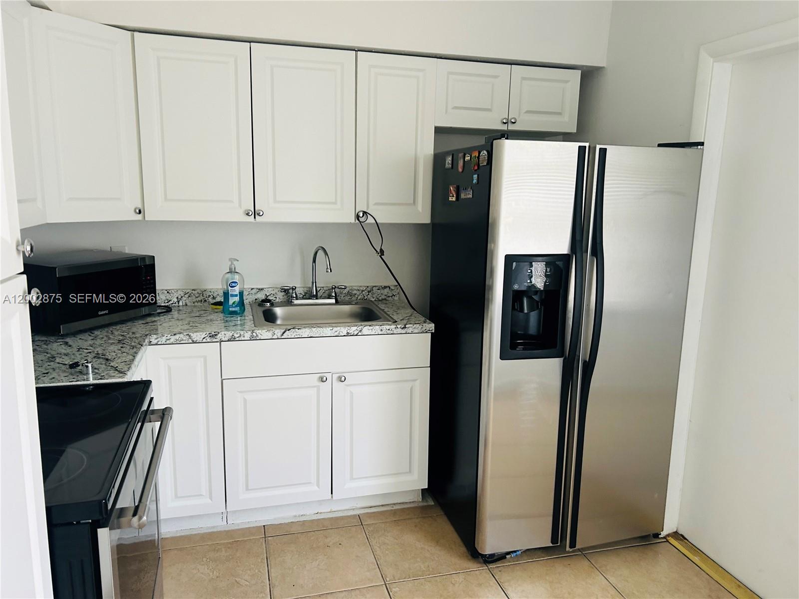 A kitchen features white cabinets, granite countertops, a stainless steel refrigerator, and a sink — 412 SW 10th St # 2, Hallandale Beach FL 33009, HALLANDALE BEACH, FL