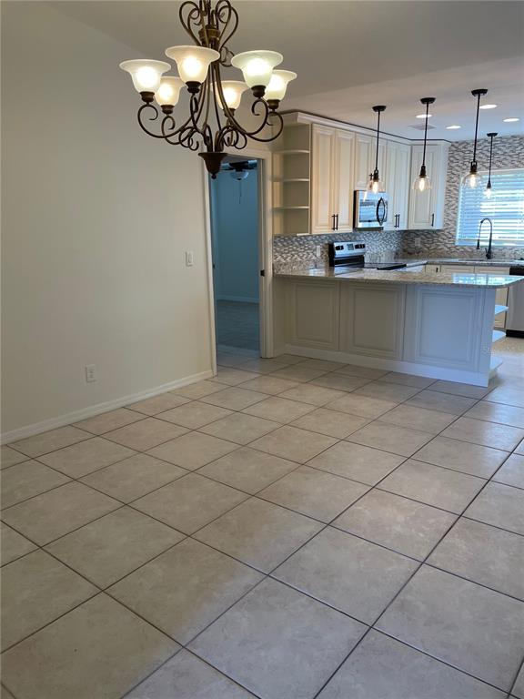 A dining area with a chandelier leads into a kitchen featuring white cabinets and tile flooring — 1424 CHESTERFIELD DRIVE, DUNEDIN, FL