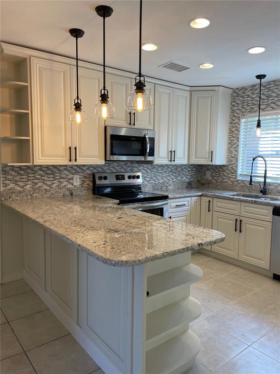 A kitchen features white cabinetry, granite countertops, a tiled backsplash, and three hanging pendant lights — 1424 CHESTERFIELD DRIVE, DUNEDIN, FL