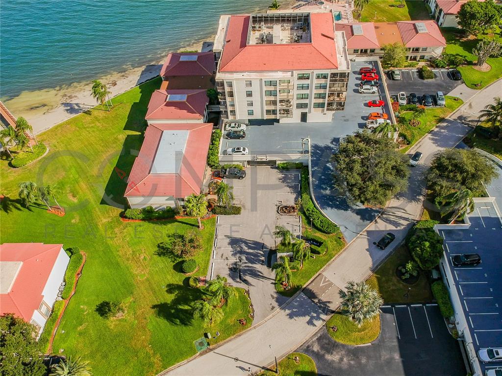 An aerial view shows a multi-story building with a red roof beside a waterfront — 6177 SUN BOULEVARD UNIT 606, ST PETERSBURG, FL