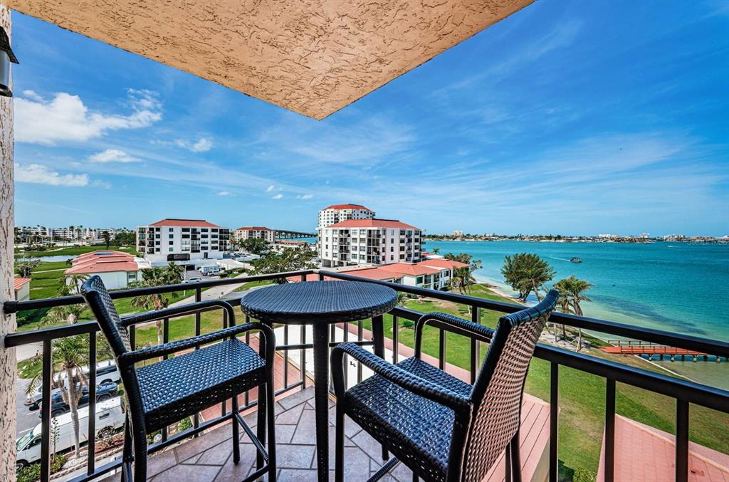 A balcony with a small table and two chairs overlooks a bay and apartment buildings — 6177 SUN BOULEVARD UNIT 606, ST PETERSBURG, FL