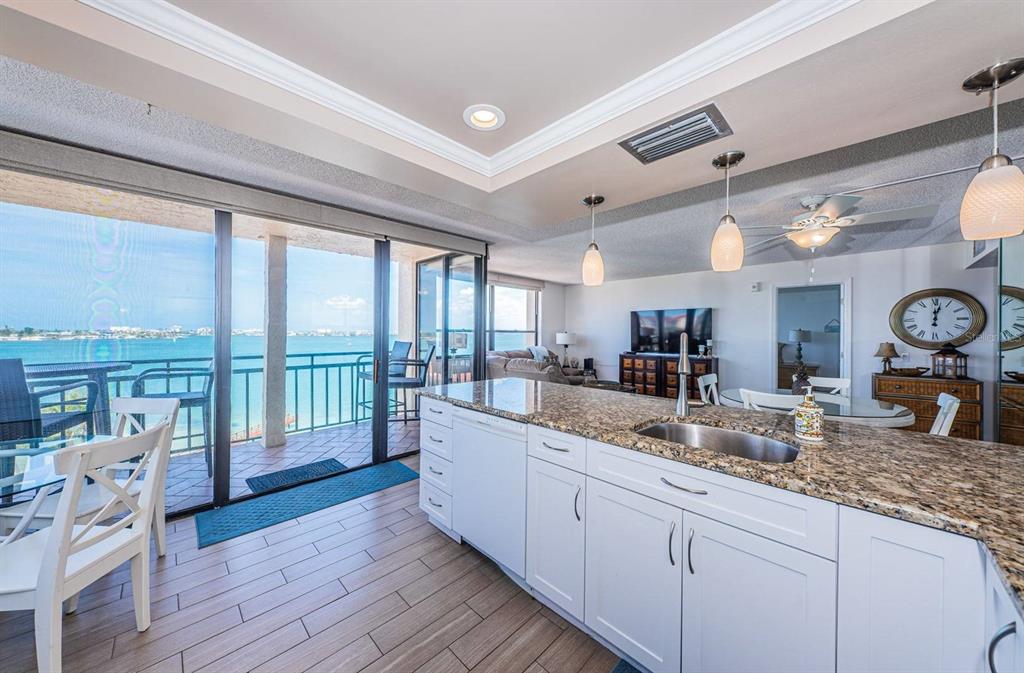 A kitchen with white cabinets and granite countertops overlooks a balcony with a water view — 6177 SUN BOULEVARD UNIT 606, ST PETERSBURG, FL