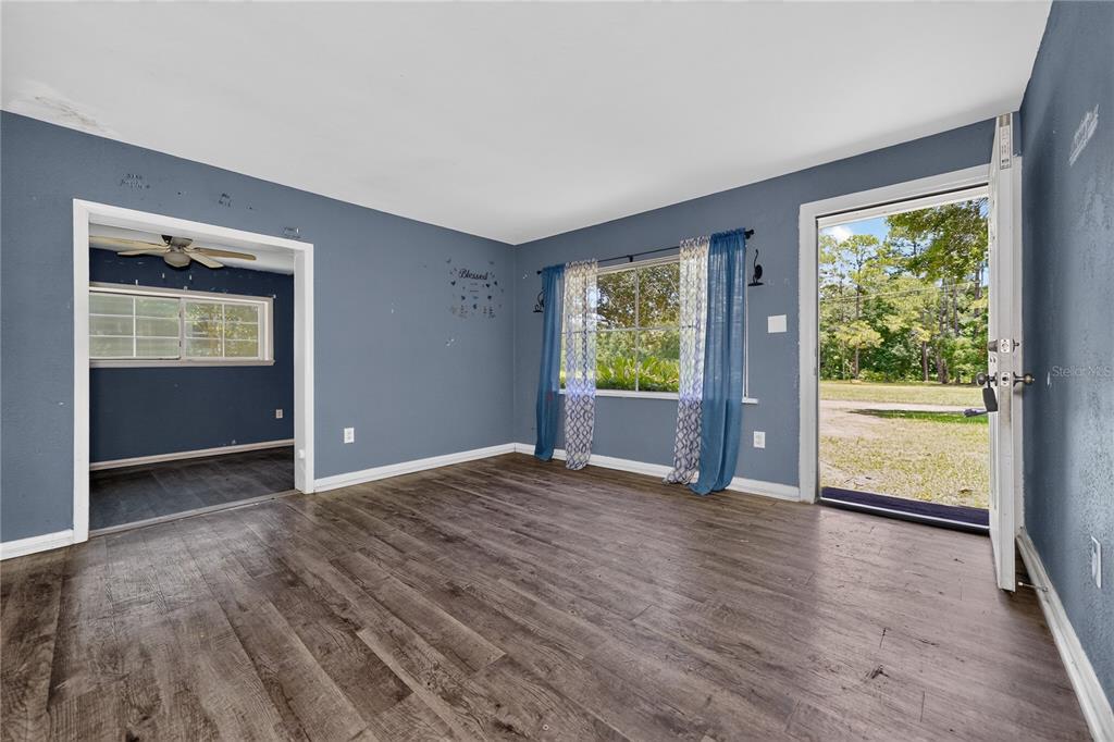 A living room with blue walls, wood-look flooring, a window with curtains, and an open door — 1510 MABRY STREET, TALLAHASSEE, FL