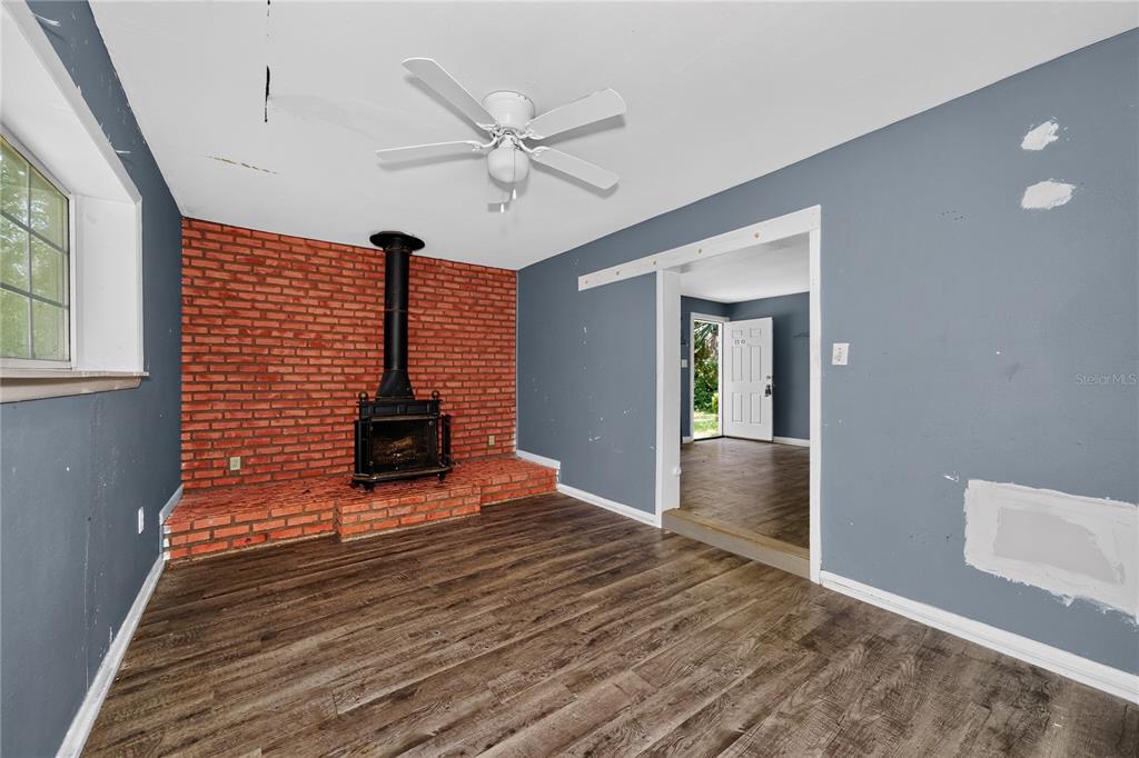 A living room features a brick fireplace with a wood stove, gray walls, and wood flooring — 1510 MABRY STREET, TALLAHASSEE, FL