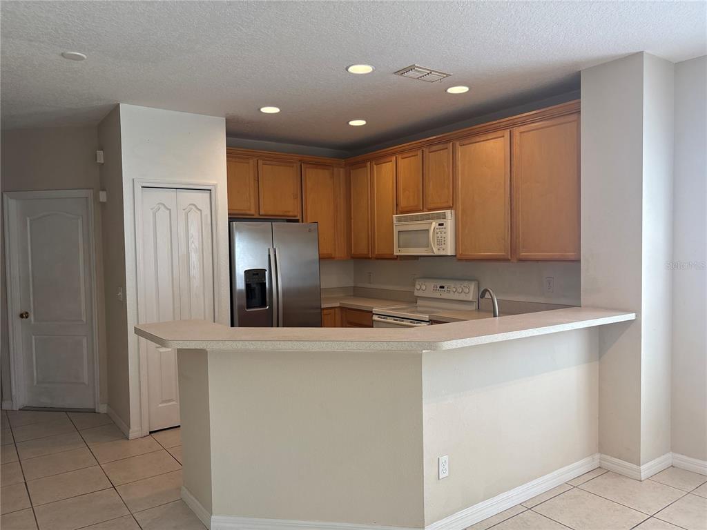 A kitchen features light wood cabinets, stainless steel appliances, and a breakfast bar counter — 9428 FLOWERING COTTONWOOD ROAD UNIT 660, ORLANDO, FL
