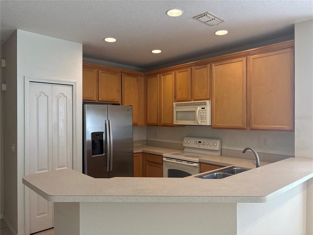A kitchen features light wood cabinets, stainless steel appliances, and a beige laminate breakfast bar — 9428 FLOWERING COTTONWOOD ROAD UNIT 660, ORLANDO, FL