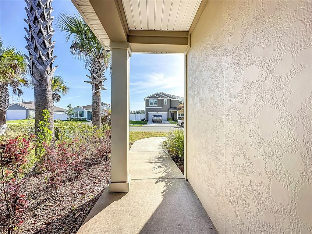A concrete walkway leads from a covered porch toward a suburban street and neighboring houses — 6214 WILD MUSTANG TRAIL, JACKSONVILLE, FL