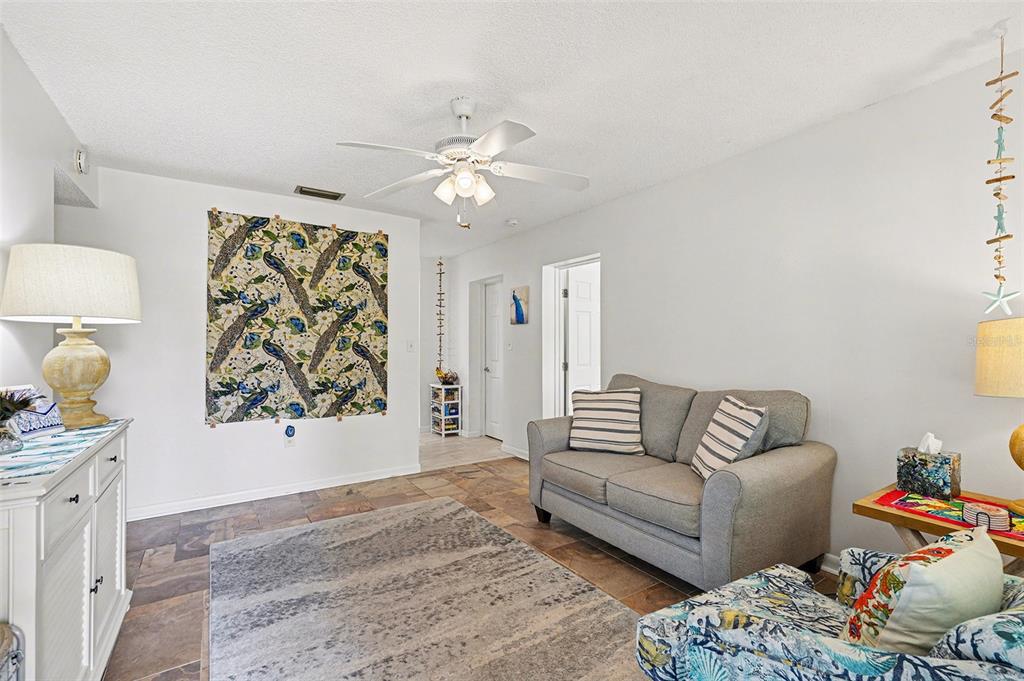 A living room with tile floors, a gray sofa, a ceiling fan, and peacock-patterned wall art — 206 HARBOR DRIVE, CAPE CANAVERAL, FL