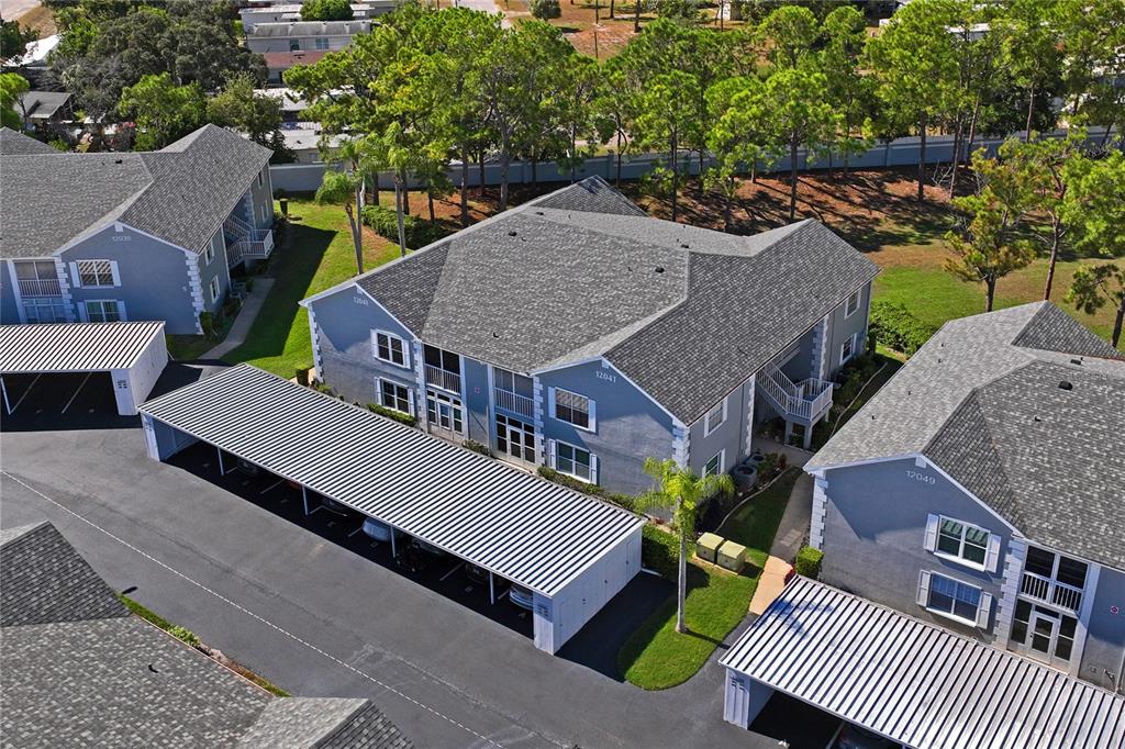 An aerial view shows apartment buildings with gray siding, shingled roofs, and covered parking structures — 12041 HOOSIER COURT UNIT 202, HUDSON, FL