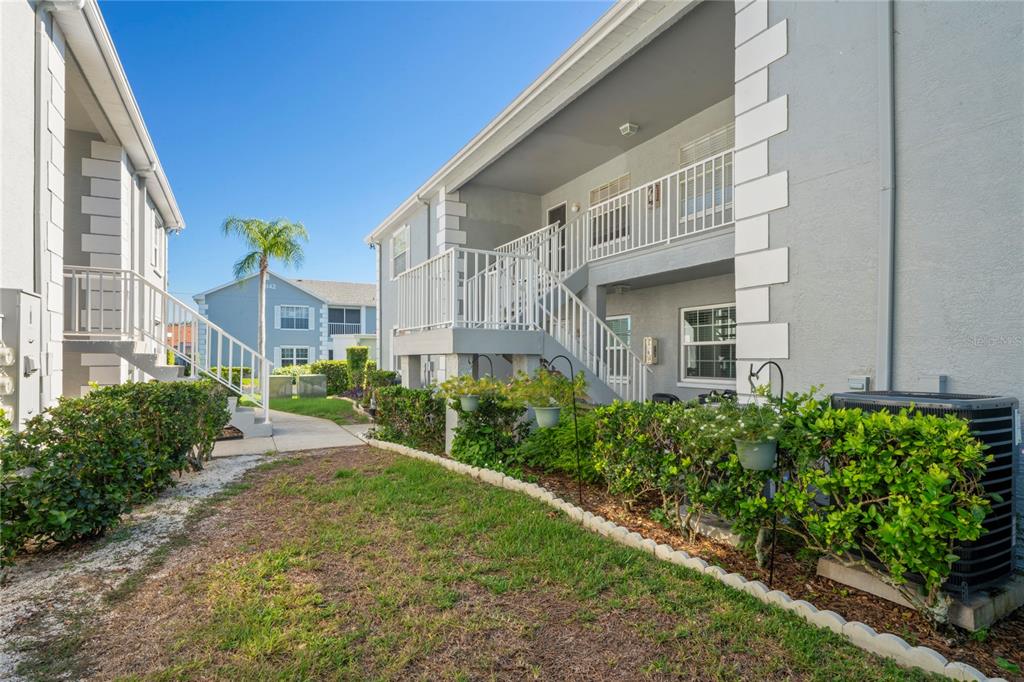 Exterior view of two-story apartment buildings with white railings, staircases, and landscaped green bushes — 12041 HOOSIER COURT UNIT 202, HUDSON, FL
