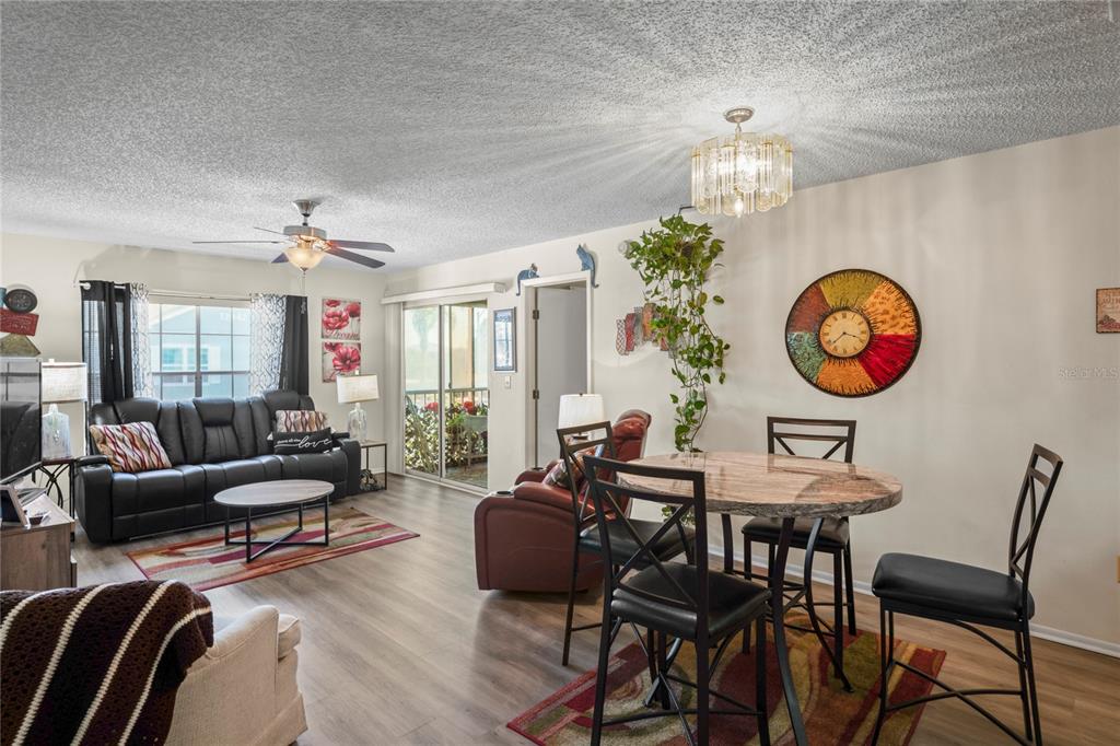 An open-concept living and dining area features wood-look flooring, a ceiling fan, and sliding doors — 12041 HOOSIER COURT UNIT 202, HUDSON, FL