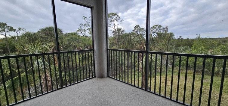 A screened-in balcony with black metal railings overlooks a dense forest and grassy area — 14161 HERITAGE LANDING BOULEVARD UNIT 1121, PUNTA GORDA, FL
