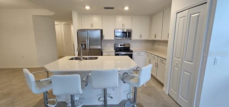A kitchen features white cabinetry, stainless steel appliances, a central island, and three bar stools — 14161 HERITAGE LANDING BOULEVARD UNIT 1121, PUNTA GORDA, FL