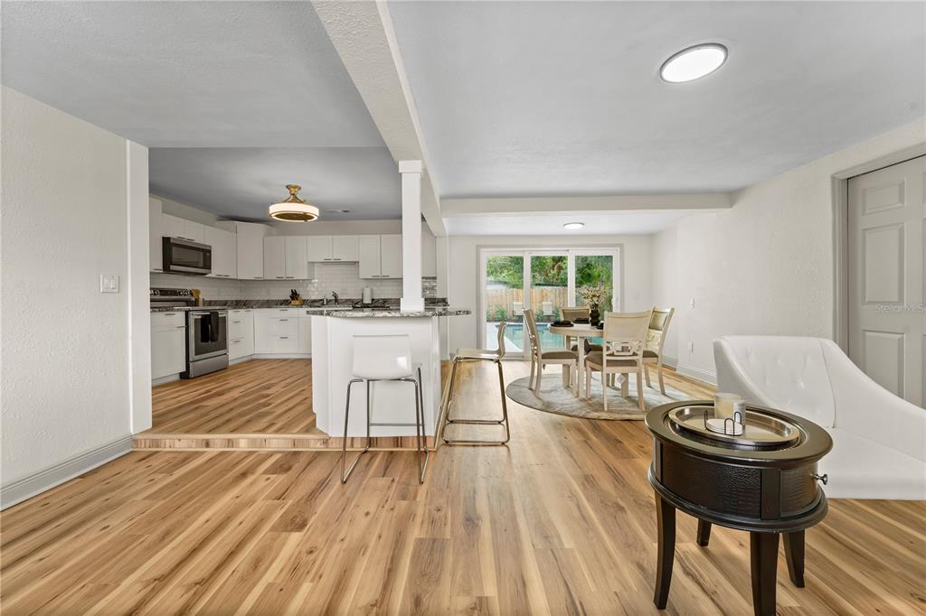 An open-concept kitchen and dining area features white cabinetry, wood-look flooring, and sliding glass doors — 7310 11TH AVENUE N, ST PETERSBURG, FL