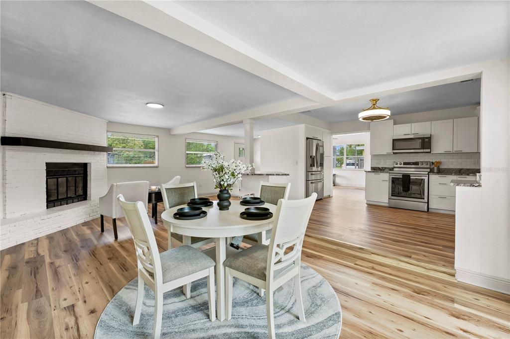 A dining area with a round table and fireplace opens into a modern white kitchen — 7310 11TH AVENUE N, ST PETERSBURG, FL